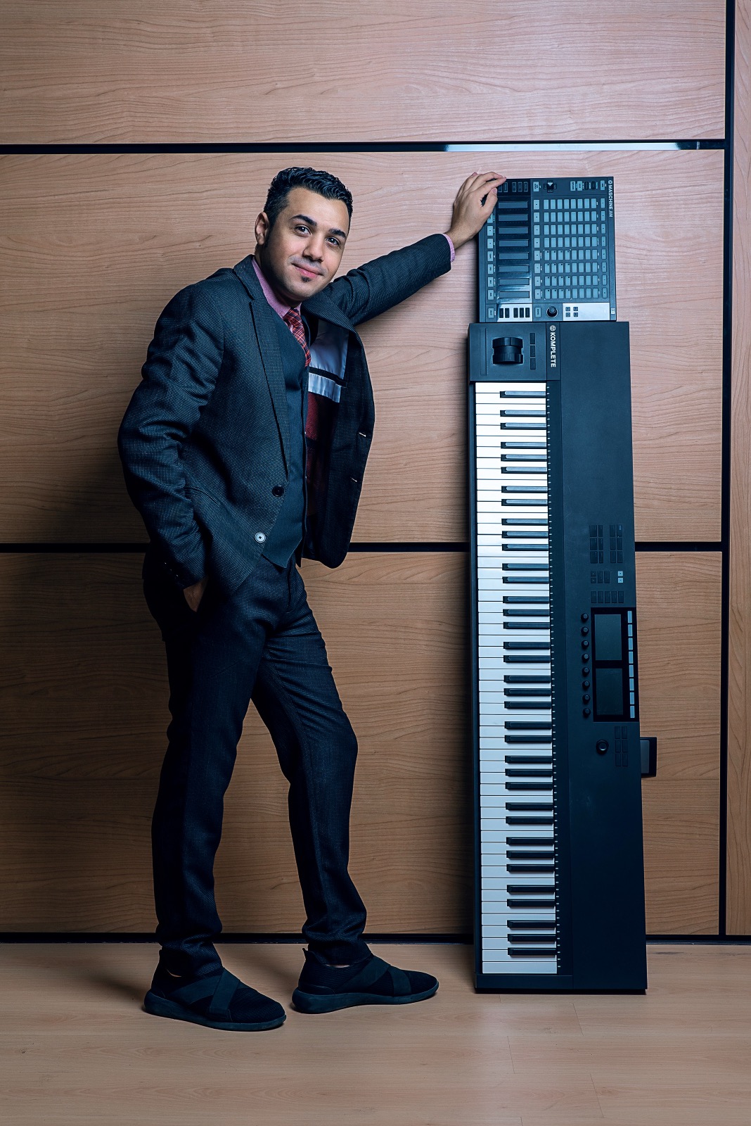 Hussain Alarab in a suit standing beside an upright synthesizer