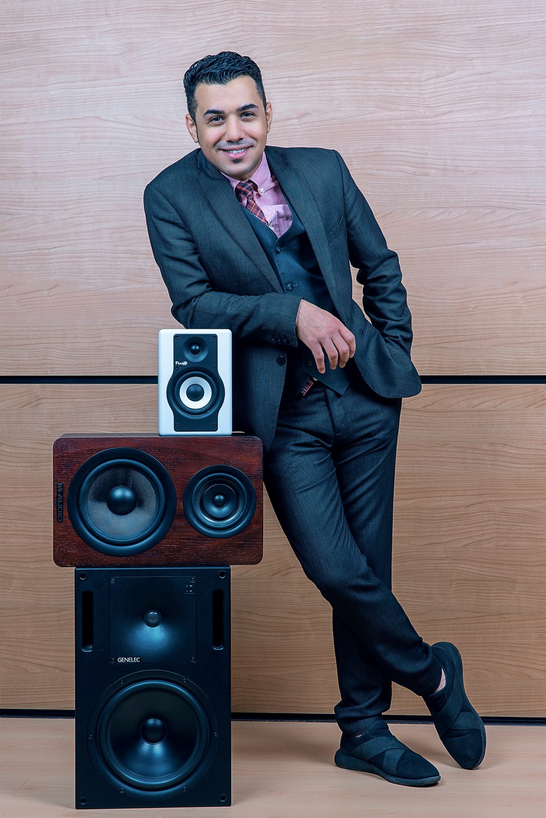 Hussain Alarab smiling in a suit beside a stack of studio monitors